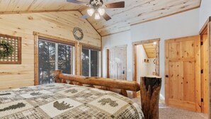 A log cabin bedroom with a wooden bed, a ceiling fan, and large windows. - The Black Bear Escaped! Hot Tub, Fire Pit , Yellowstone, Golf Course! (Island Park)
