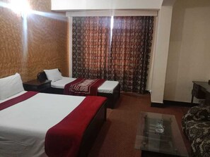 Two beds, a sofa, and a coffee table in a cozy room with a large window and patterned curtains.