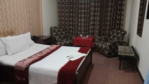 A hotel room with a bed, a sofa, a small table, and a patterned curtain. - Hotel Al Badar (Rawalpindi)