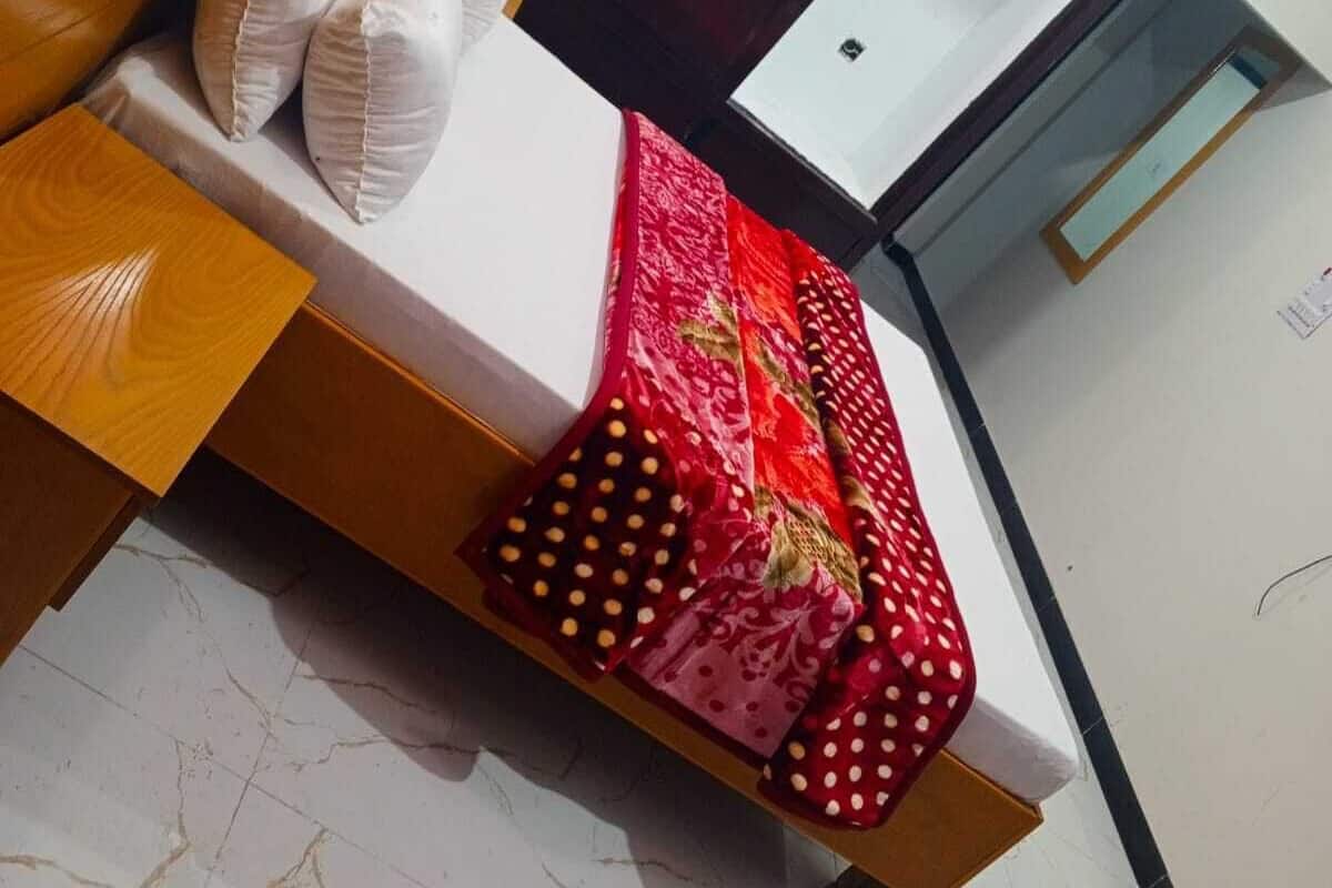 A bed with a wooden headboard, white pillows, and a red patterned bedspread.