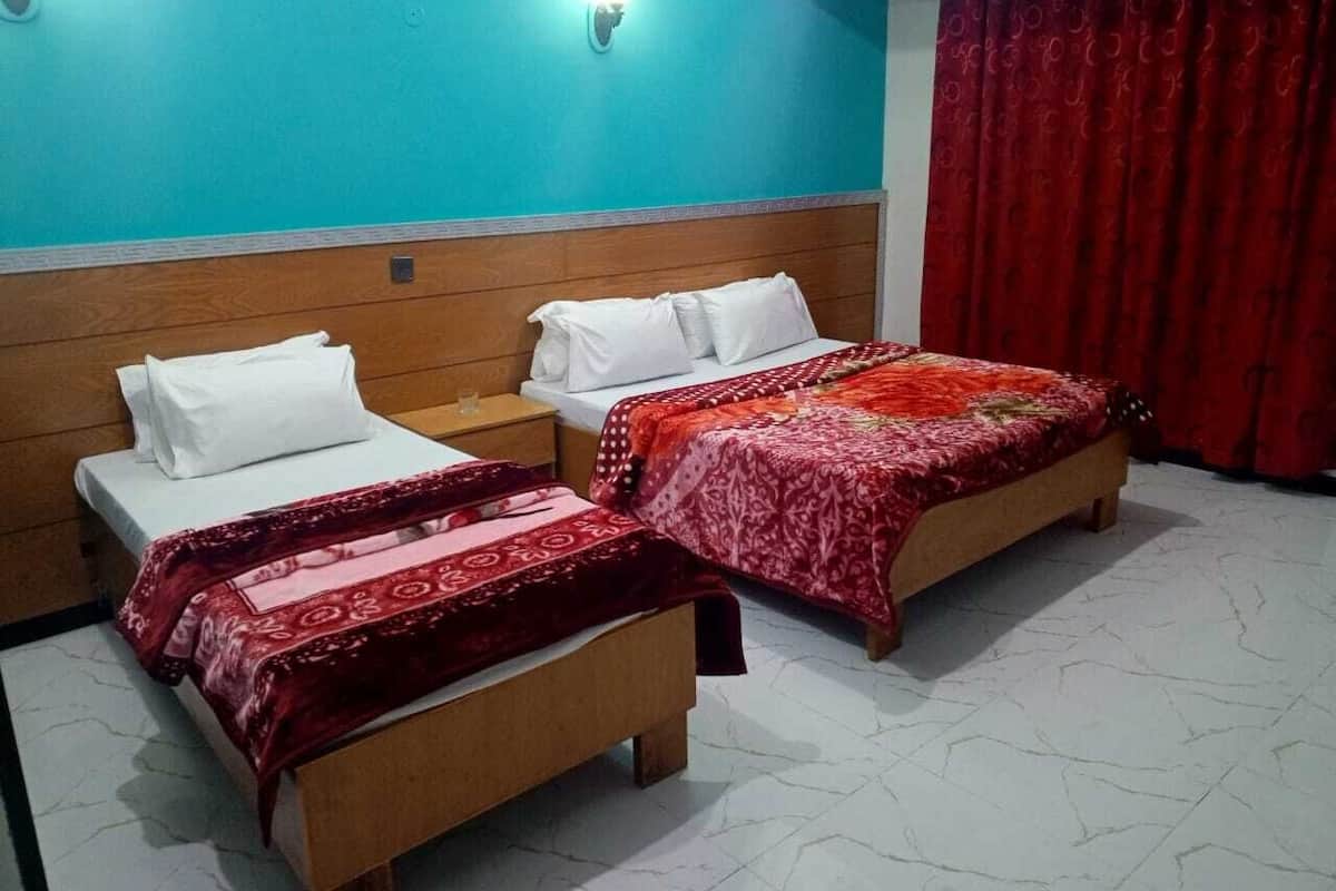 A hotel room with two beds, each with a wooden headboard and white bedding. There are two wall-mounted lights and a red curtain.
