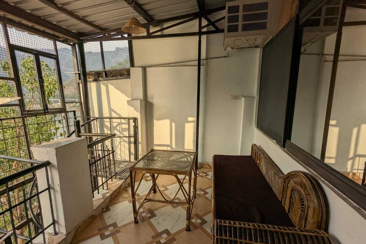 A balcony with a metal railing, a wicker bench, a glass table, and a large window.