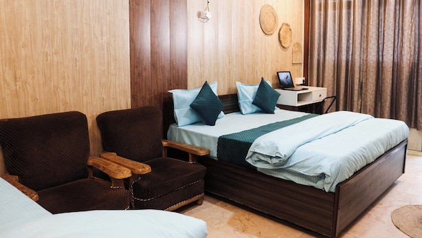 Una habitación con una cama, dos sillones, un escritorio pequeño y un aire acondicionado de pared.