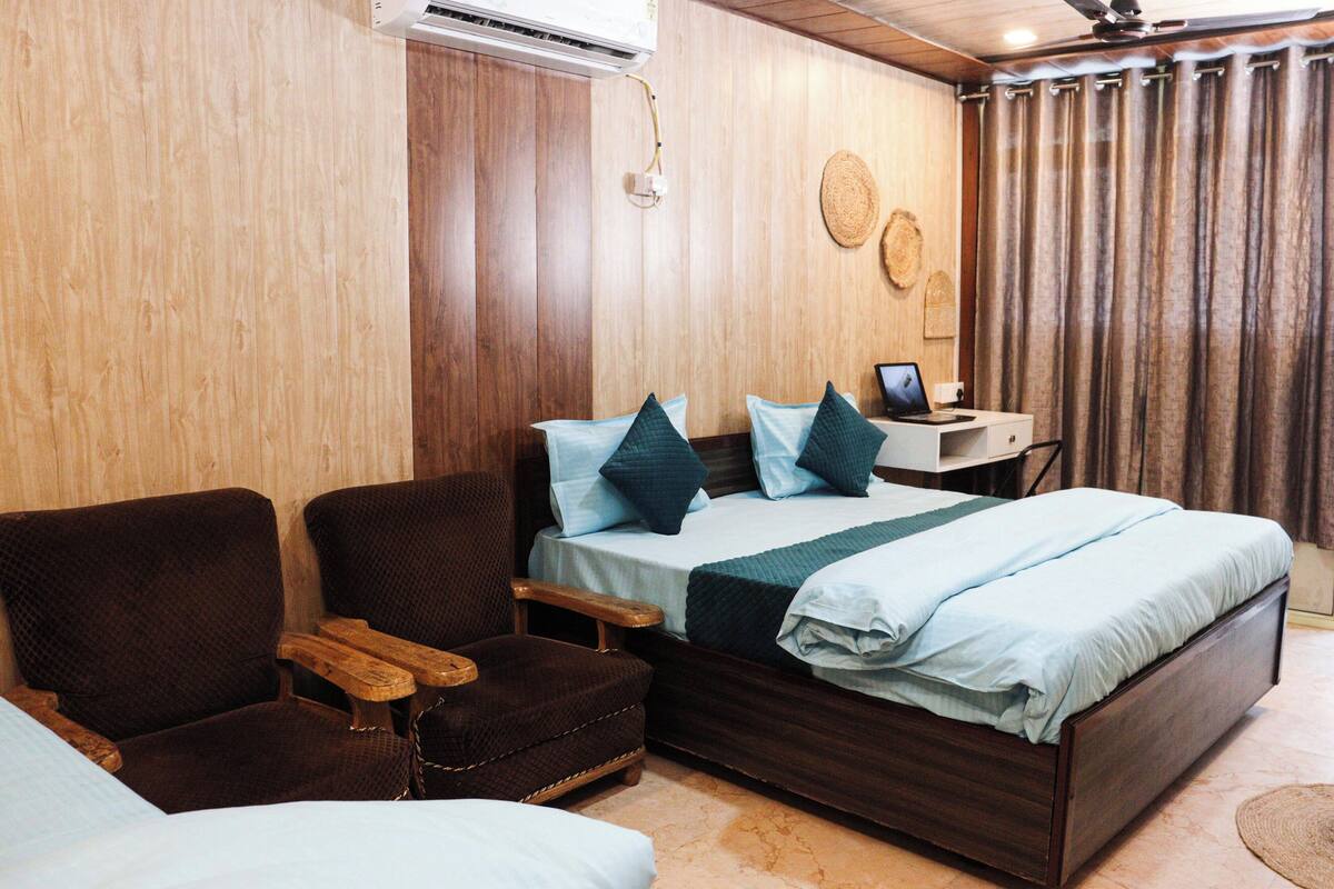 A room with a bed, two armchairs, a small desk, and a wall-mounted air conditioner.