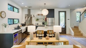 A modern kitchen with a central island, stainless steel appliances, and a dining area with a wooden table and chairs. - Mill Creek by AvantStay | Modern Design, Patio, Hot Tub (Healdsburg)