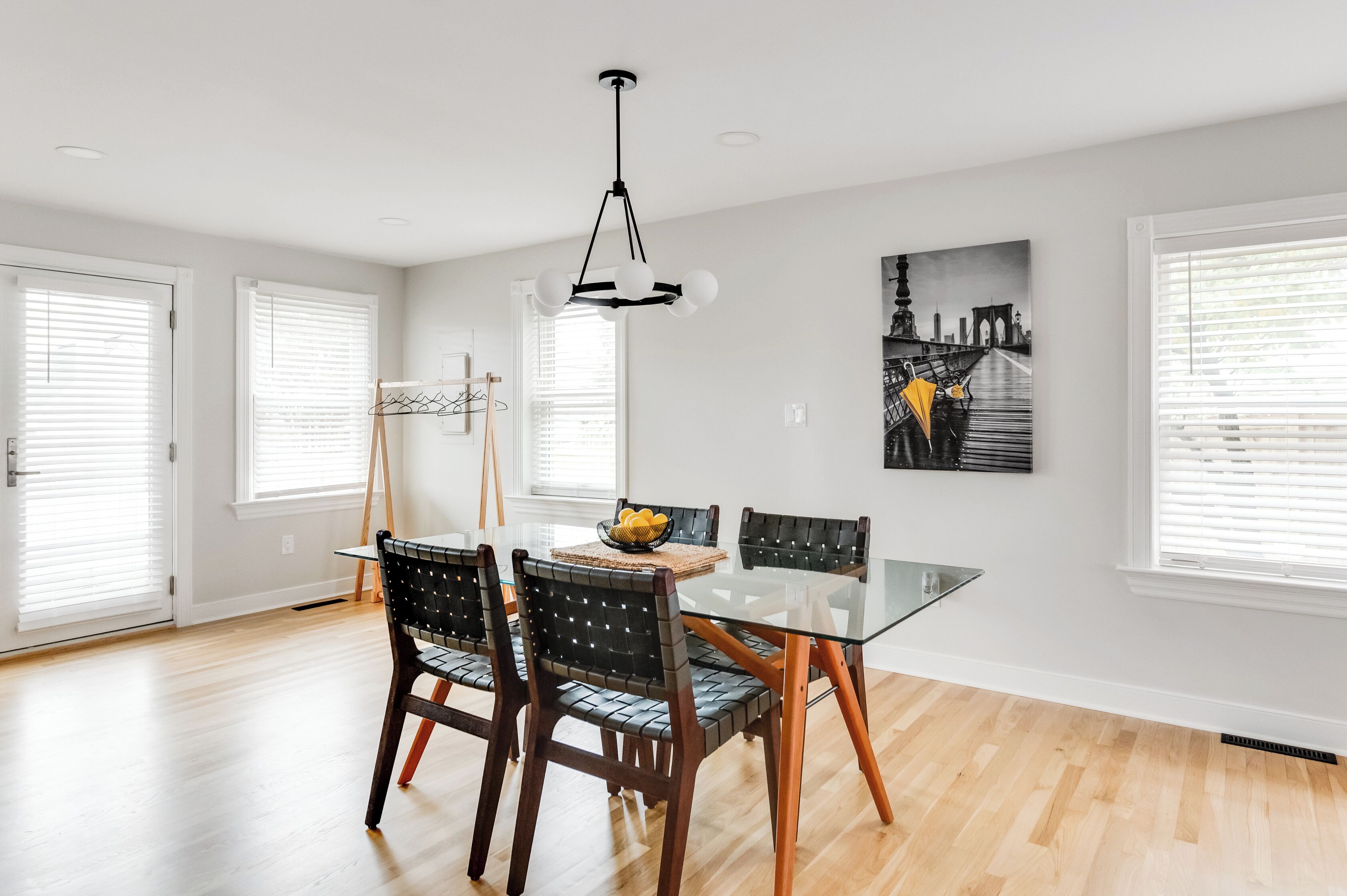 A dining area with a glass table, wooden chairs, and a modern pendant light.