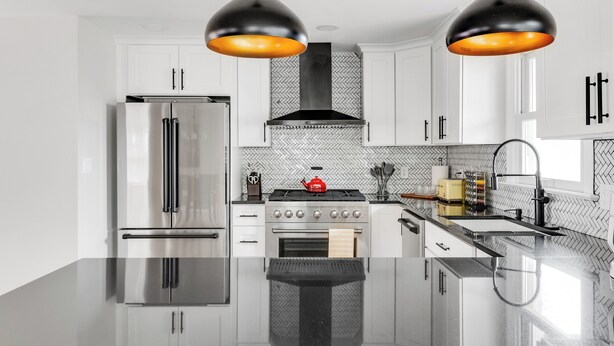 A modern kitchen with stainless steel appliances, a herringbone-patterned backsplash, and pendant lighting.