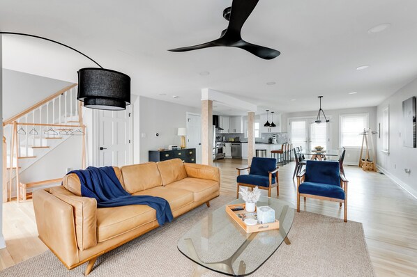 Ein modernes Wohnzimmer mit einer Ledersofa, einem Glastisch und einem Essbereich mit blauen Stühlen.