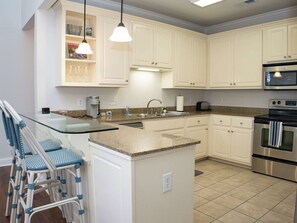 A kitchen with white cabinets, a granite countertop, a stainless steel oven, and a glass island with bar stools.