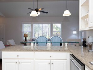 A kitchen with a glass-top island, white cabinetry, a ceiling fan, and a dining area with chairs and a table.