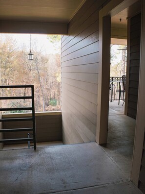 A covered porch with a metal railing, a concrete floor, and a view of trees outside.
