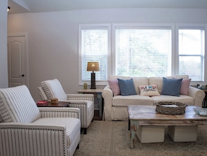 Un salon avec des fauteuils à rayures, un canapé avec des coussins, une lampe et une table sur laquelle se trouve un panier.