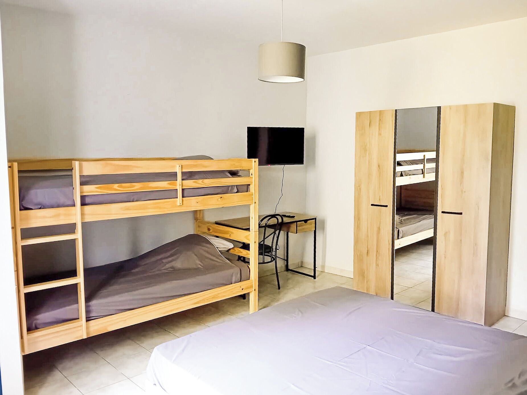 A bunk bed with a desk and a TV, a wardrobe, and a hanging light fixture.