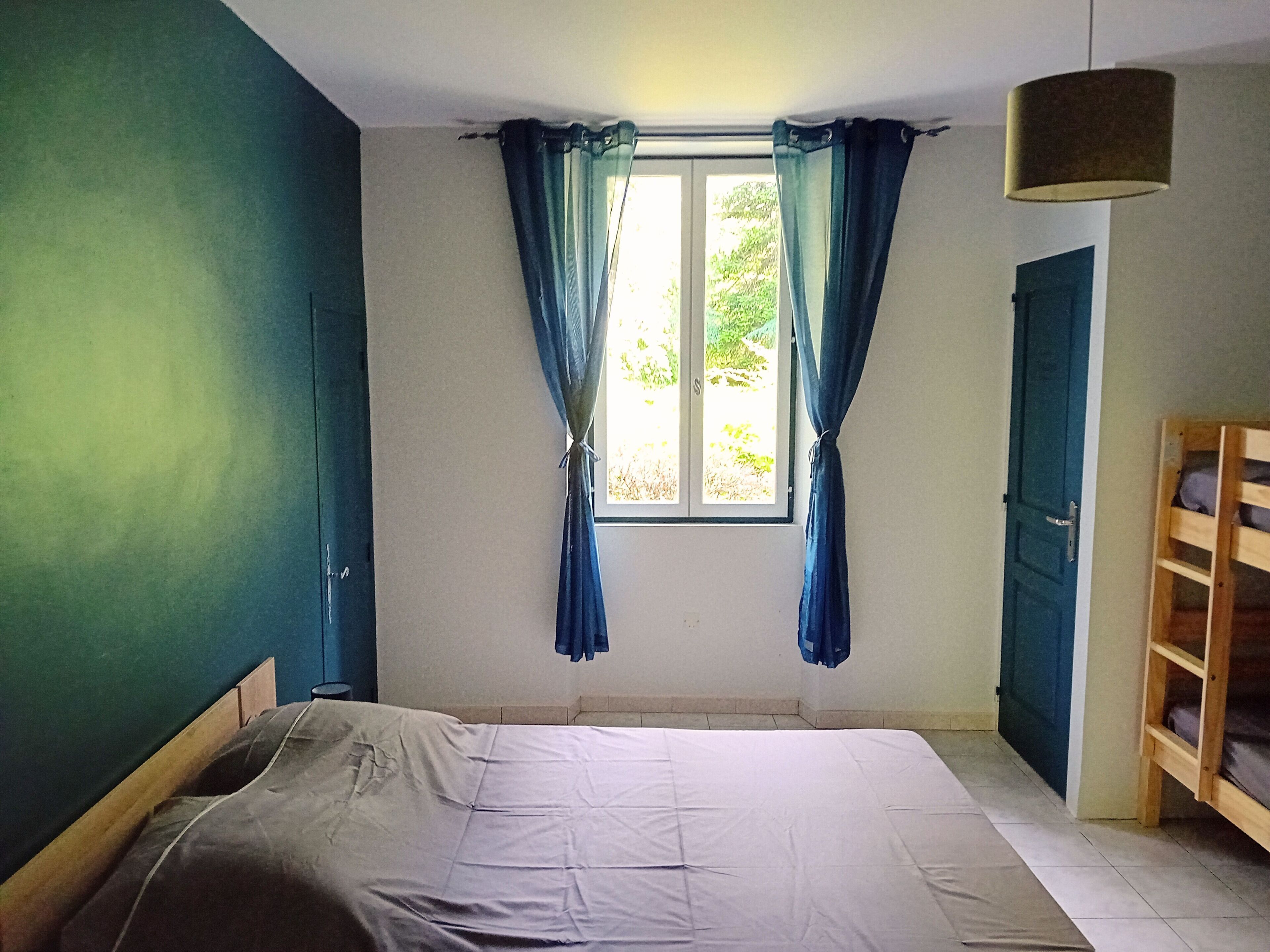 A bedroom with a bed, a window with curtains, a door, and a wooden bench.