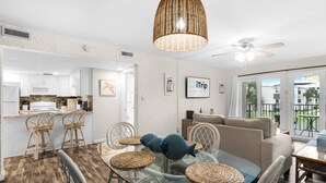A modern kitchen with white cabinets, a microwave, and a stove. There is a dining area with a glass table and wicker chairs. A ceiling fan and pendant light are visible. - Spacious updated condo with a lake view, private balcony, and $300 Free Activities Daily! (Panama City Beach)