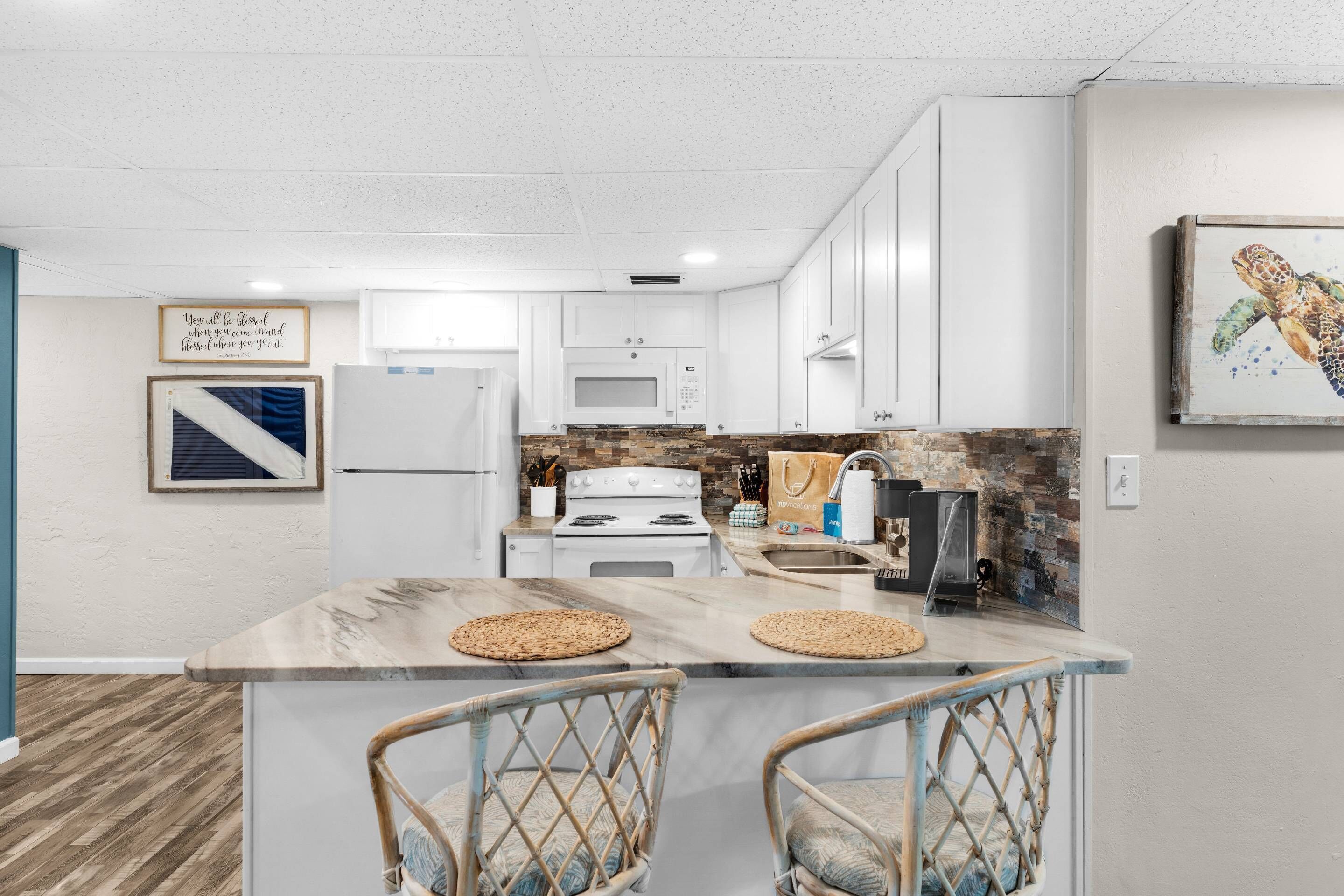 A modern kitchen with white cabinets, a central island with two chairs, a microwave, stove, and a sink.