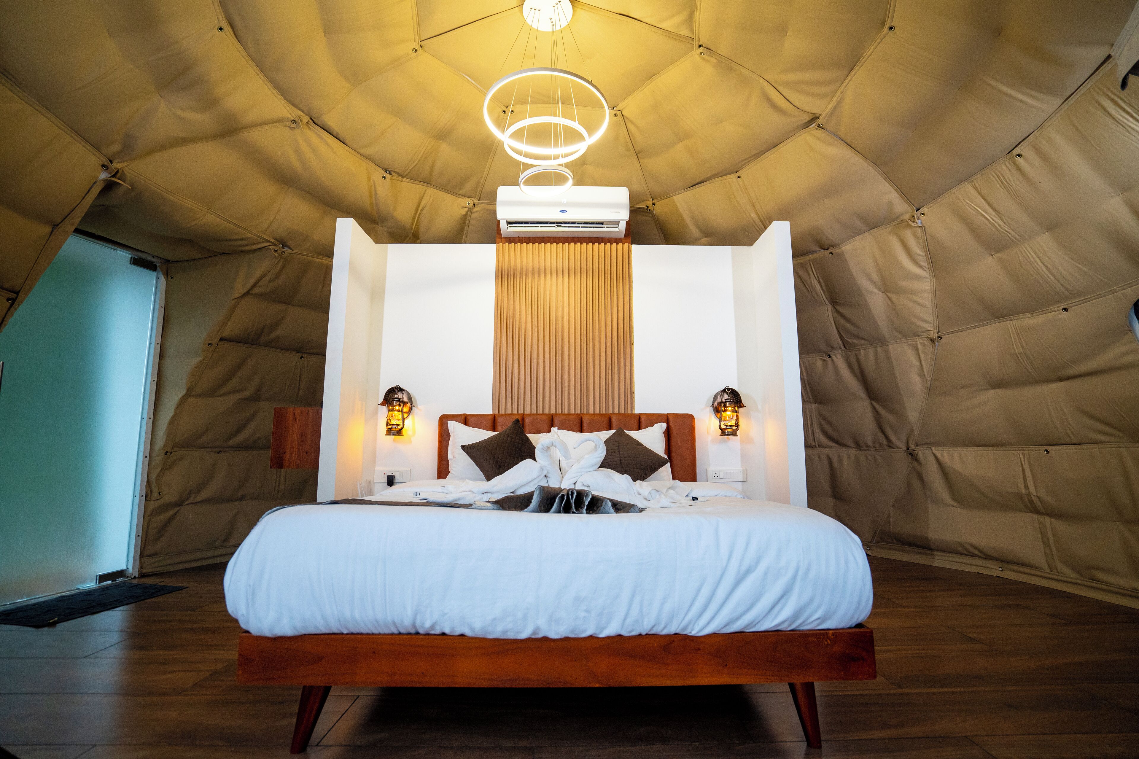 A spacious tented room with a large bed, a ceiling fan, and two wall-mounted lamps.