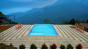 A rectangular pool with a metal ladder, surrounded by a tiled deck with benches. - Nexstay Karimb Resorts (Thamarassery)