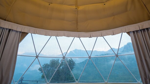 A tented room with a bed, two chairs, a table, and a large window offering a view of mountains. - Nexstay Karimb Resorts (Thamarassery)
