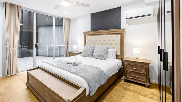 A modern bedroom with a large bed, a ceiling fan, an air conditioning unit, a sliding glass door, and a wooden nightstand.