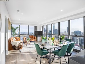 Ein modernes Wohnzimmer mit Essbereich, großen Fenstern und Blick auf die Stadt.
