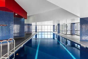 Une piscine intérieure moderne, avec des carreaux bleu clair, un long plongeoir et un banc.