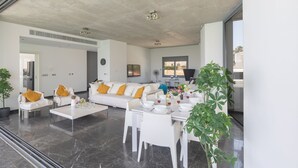 A spacious living area with a white sofa set, a dining table with chairs, and a large window providing natural light. - Sea front Elegant villa HEATED private POOL in Fig Tree Bay Protaras
  - 5 bedrm (Protaras)