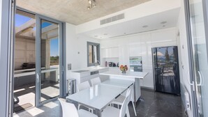 A modern kitchen with white cabinetry, a large island, and a sliding glass door leading to an outdoor area. - Sea front Elegant villa HEATED private POOL in Fig Tree Bay Protaras
  - 5 bedrm (Protaras)
