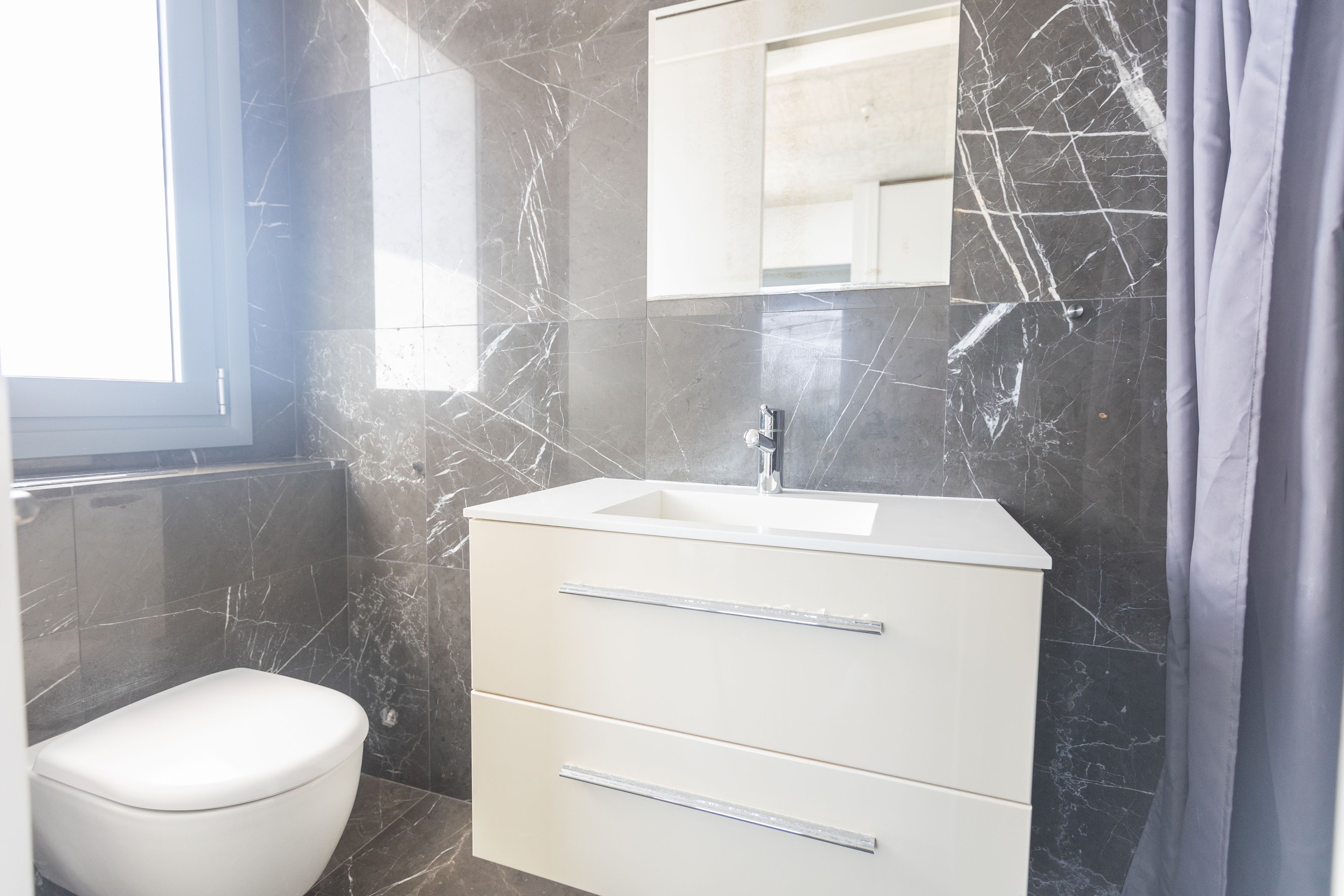 Un baño con inodoro blanco, lavabo y espejo.
