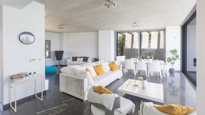 A modern living room with a white sofa, yellow cushions, a coffee table, and a dining area with white chairs. - Sea front Elegant villa HEATED private POOL in Fig Tree Bay Protaras
  - 5 bedrm (Protaras)
