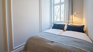A bedroom with a bed, a window with curtains, and a bedside lamp.