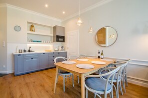 Una cocina moderna con armarios grises, una mesa de comedor de madera con manteles individuales blancos y un espejo redondo en la pared.