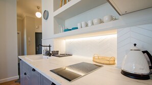 A modern kitchen with a white countertop, a built-in stove, a coffee maker, and a basket.
