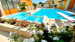 Une piscine dotée d’une terrasse ensoleillée, entourée de plantes et de fleurs en pot.