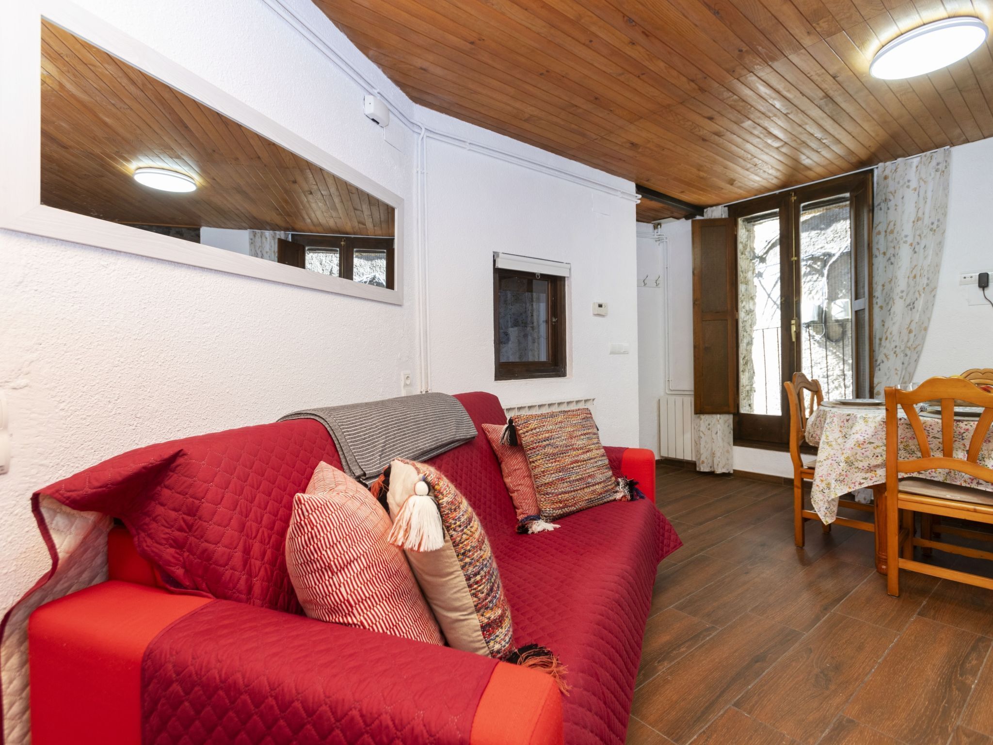 A cozy room with a red sofa, wooden flooring, and a small table with chairs.