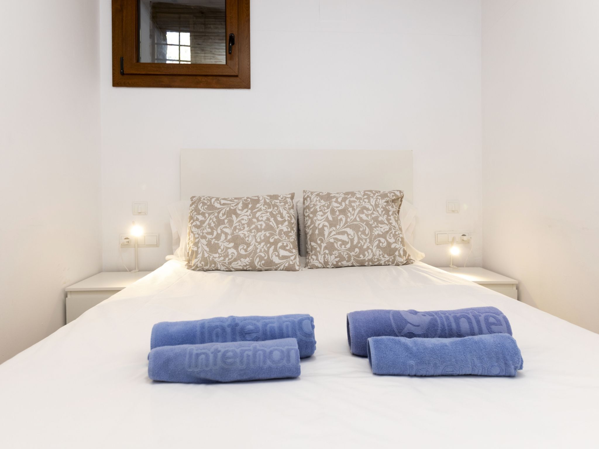 A neatly made bed with two decorative pillows and three folded towels.