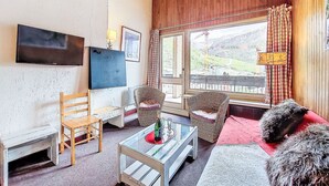 Una sala de estar acogedora con techo de madera, un televisor de pantalla plana en la pared, mobiliario de mimbre y vistas a un paisaje montañoso a través de un ventanal grande.