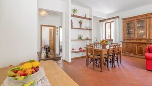 A dining area with a wooden table and chairs, a fruit bowl, and a cabinet with glass doors. - Chiara Apartment In Porta San Frediano (Florence)