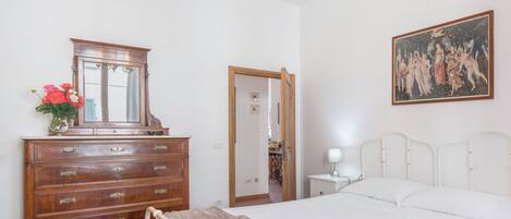 Ein Schlafzimmer mit einem hölzernen Schminktisch, einem Bett mit weißer Bettwäsche, einer Chandelieber, einem Bild an der Wand und einem Spiegel.