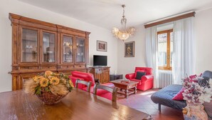 A dining area with a wooden table and chairs, a red sofa, a television, and a cabinet with glass doors. - Chiara Apartment In Porta San Frediano (Florence)