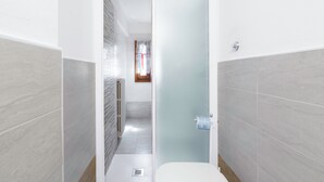 A narrow hallway with a white door leading to a bathroom. The hallway has light grey tiled walls and a white floor. - Chiara Apartment In Porta San Frediano (Florence)