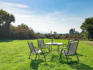 A grassy outdoor area with a table and four chairs, a bottle of wine, and a glass on the table. - Traditional style thatched cottage in Kenmare (Kenmare)