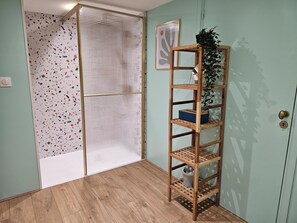 Une pièce avec un plancher en bois, une porte blanche à motifs, une étagère en bois ornée d’une plante et un tableau encadré accroché au mur.
