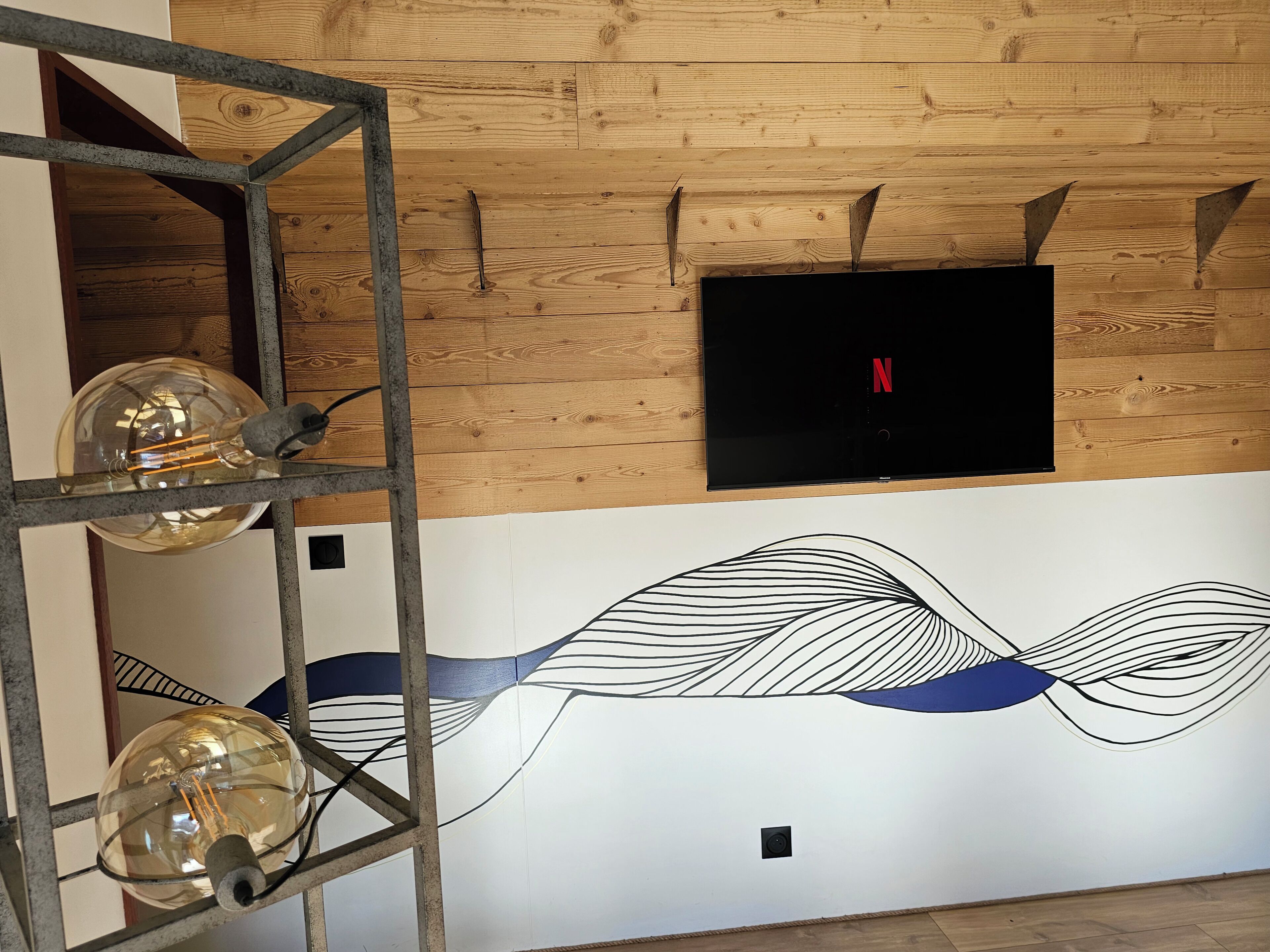 A room with a wooden ceiling, a mounted flat-screen TV, and a wall with a black and white abstract design.