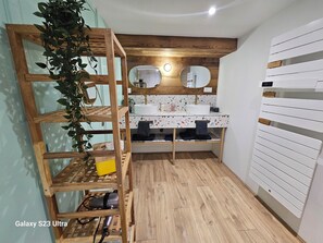 Une salle de bain avec une étagère en bois, un lavabo avec un miroir au-dessus et un porte-serviettes fixé au mur.