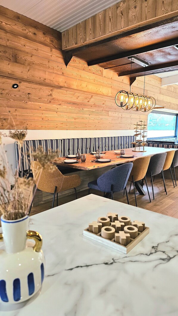 Un espace repas doté d’un plafond en bois, de banquettes à motifs rayés et d’une table en marbre agrémentée de blocs de bois.