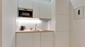 Une cuisine compacte avec des meubles blancs, un four encastré, une machine à café et un évier.