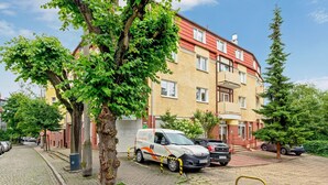 Un immeuble résidentiel avec un toit rouge, un fourgon garé et un arbre au premier plan.