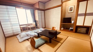Perinteinen japanilainen huone, jossa on tatamimatto, matala pöytä tyynyineen, televisio ja liukuovi.