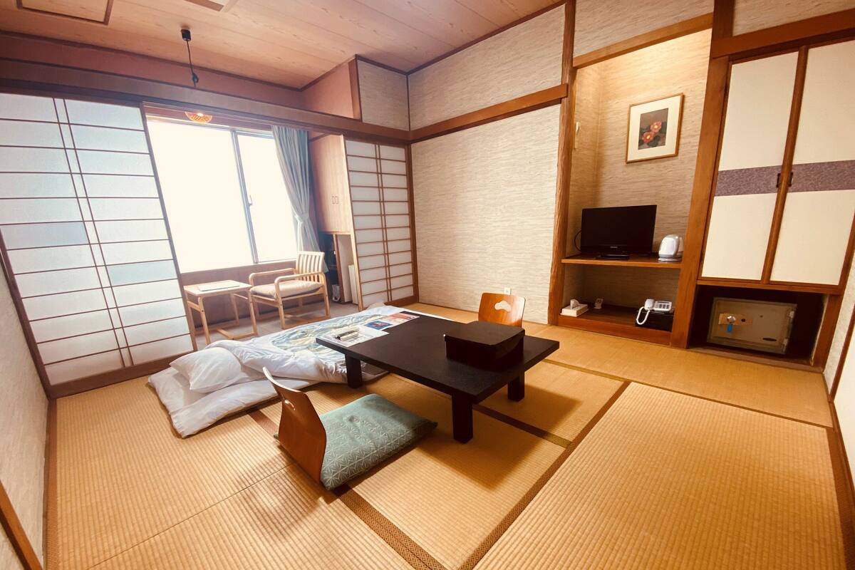 A traditional Japanese room with tatami flooring, a low table with cushions, a television, and a sliding door.